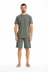Man wearing a olive green buttoned t-shirt and linen shorts on a white background