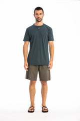Man wearing a ocean blue buttoned t-shirt and linen shorts on a white background