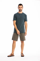 Man wearing a ocean blue buttoned t-shirt and linen shorts on a white background