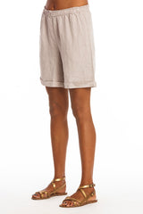 A model wearing long beige linen shorts with pockets and a pair of sandals.