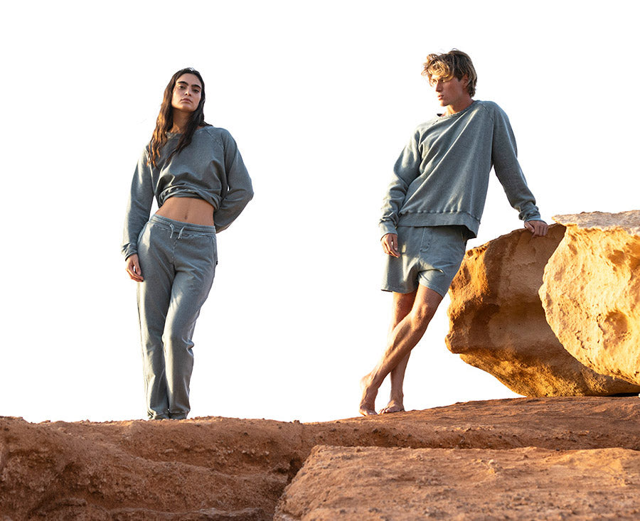 Two people wearing matching gray outfits standing on a rocky landscape.