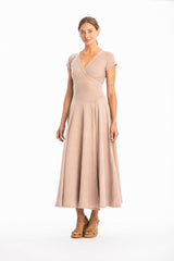 Woman wearing a long V-neck light brown dress with short sleeves on a white background